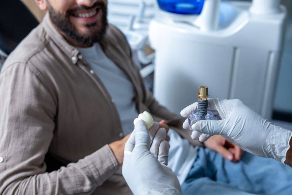 Ein lächelnder Patient bei der Beratung zur Zahnimplantologie in Essen, während der Zahnarzt ein Implantatmodell präsentiert.