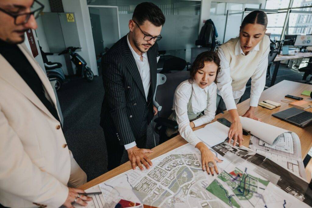 Vier Personen diskutieren einen Stadtplan mit Fokus auf Parkbank-Standorten in einem Buero fuer Freiraumplanung