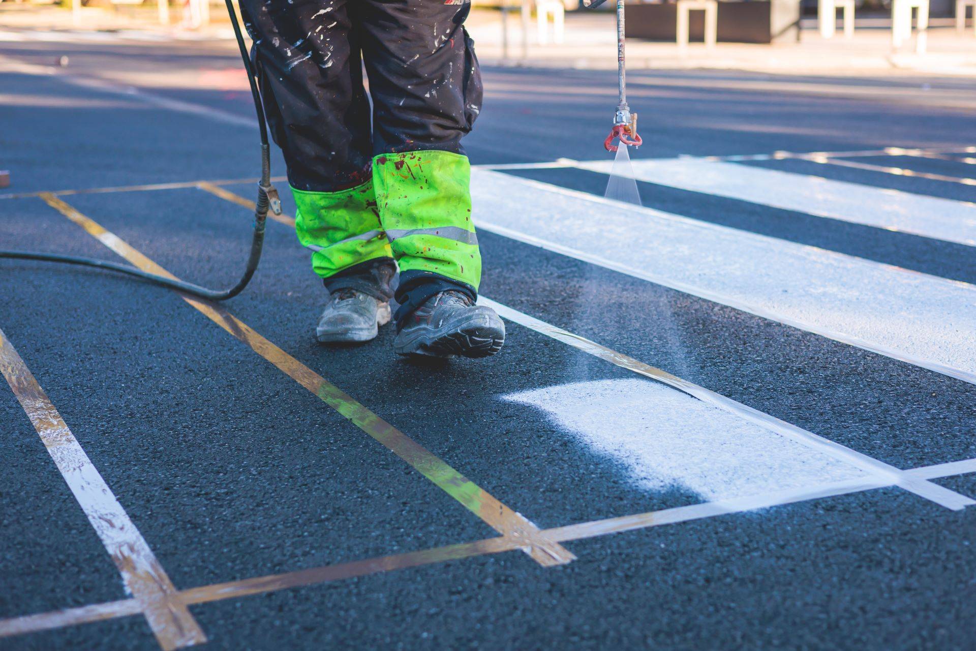 Arbeiter trägt weiße Fahrbahnmarkierung mit Sprühgerät auf