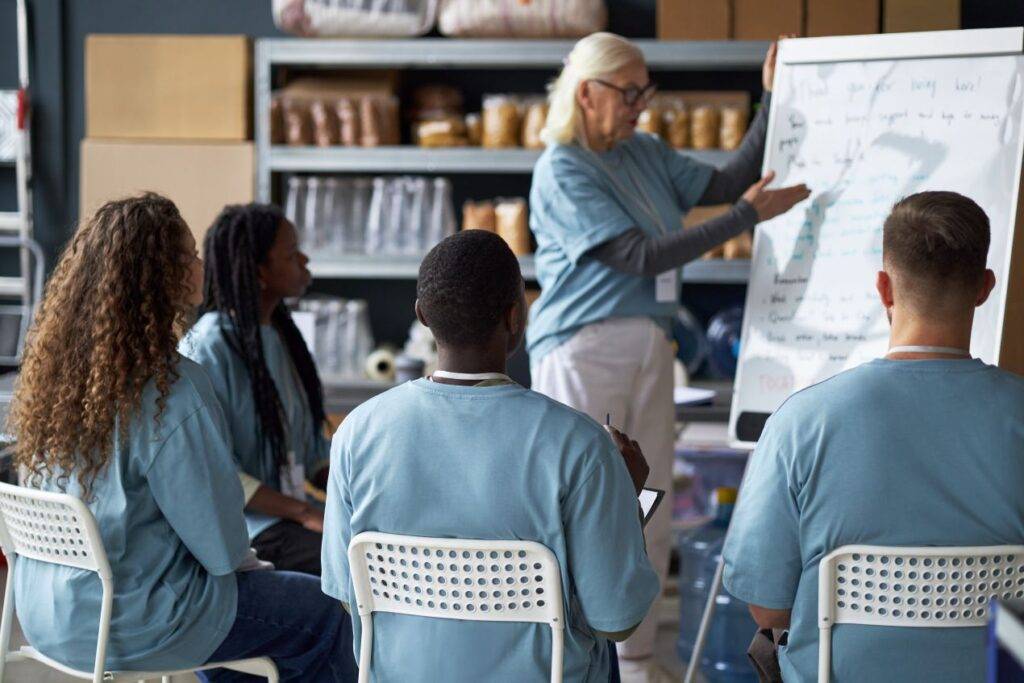 Eine Gruppe von Erwachsenen in blauen Uniformen nimmt an einer Schulung teil, waehrend eine Person am Flipchart erklaert – Symbol fuer Weiterbildung und Strukturwandel bei Quereinsteiger Kindergarten.